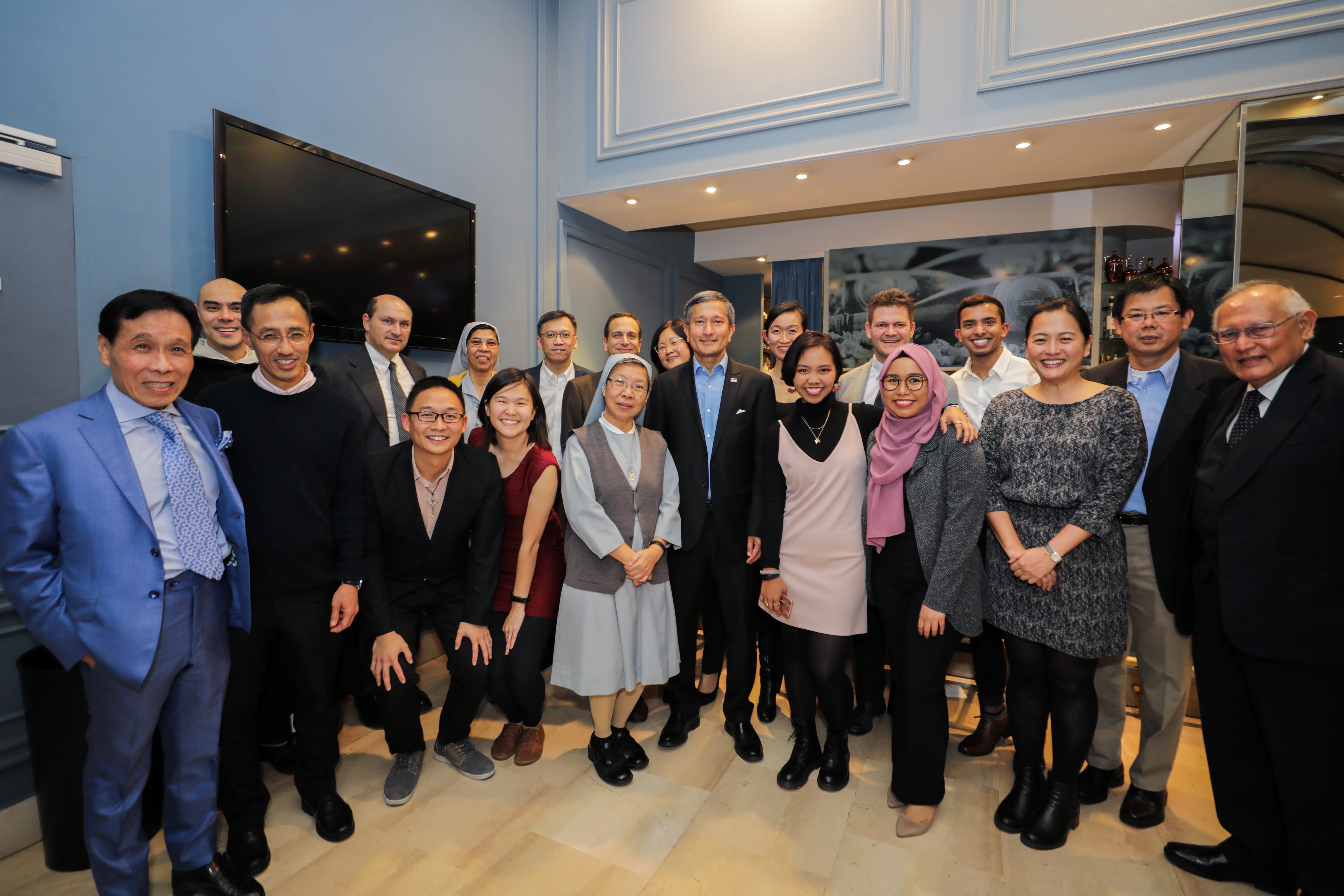 Group portrait of diverse people in formal attire, including two nuns, standing in a well-lit room.